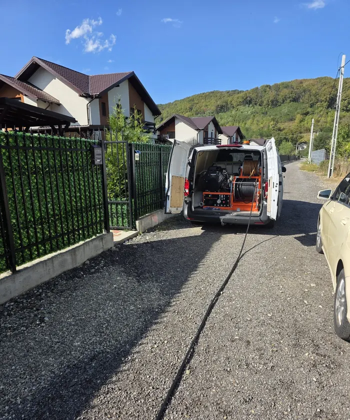 Autoutilitara parcată pe o stradă de deal, cu furtunul întins până la căminul unei case